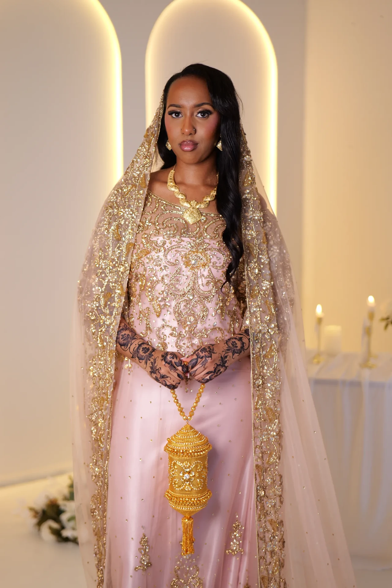 Front view of a blush dirac with gold embroidery and a matching veil