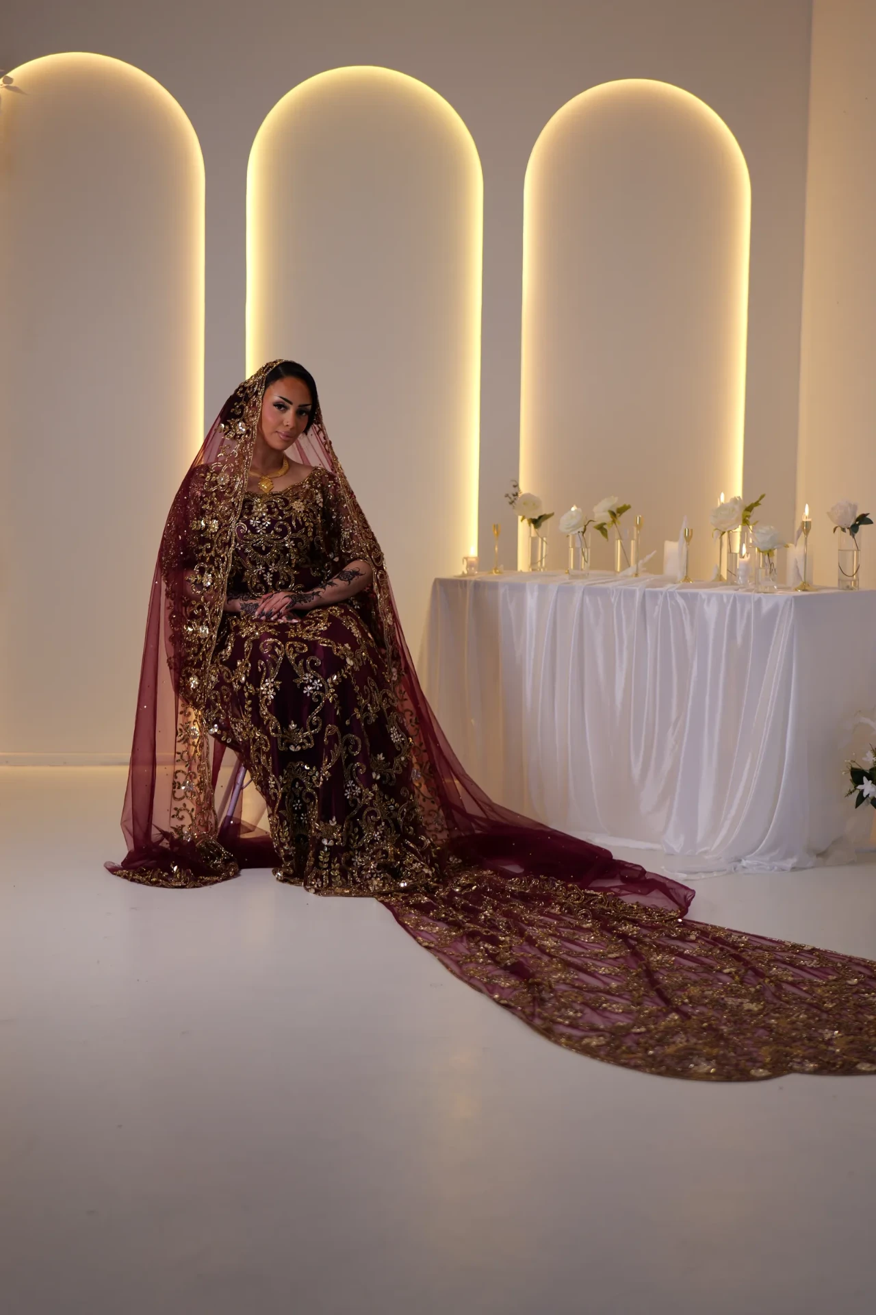 Wine bridal look with a long train beneath warm illuminated arches