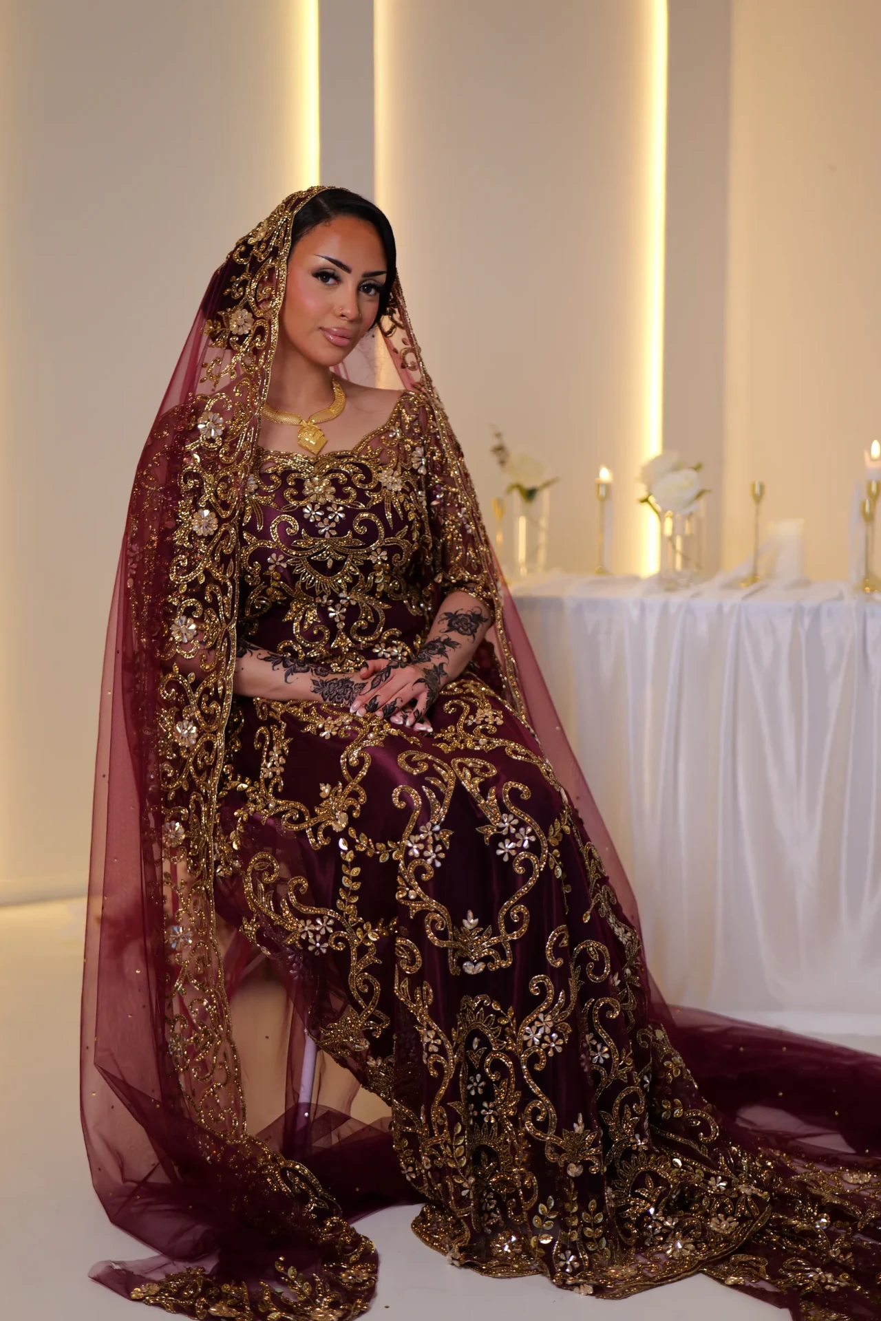 Seated model wearing a wine dirac and an embroidered burgundy veil